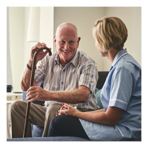 Smiling retired senior man sitting on sofa with female home carer at care home