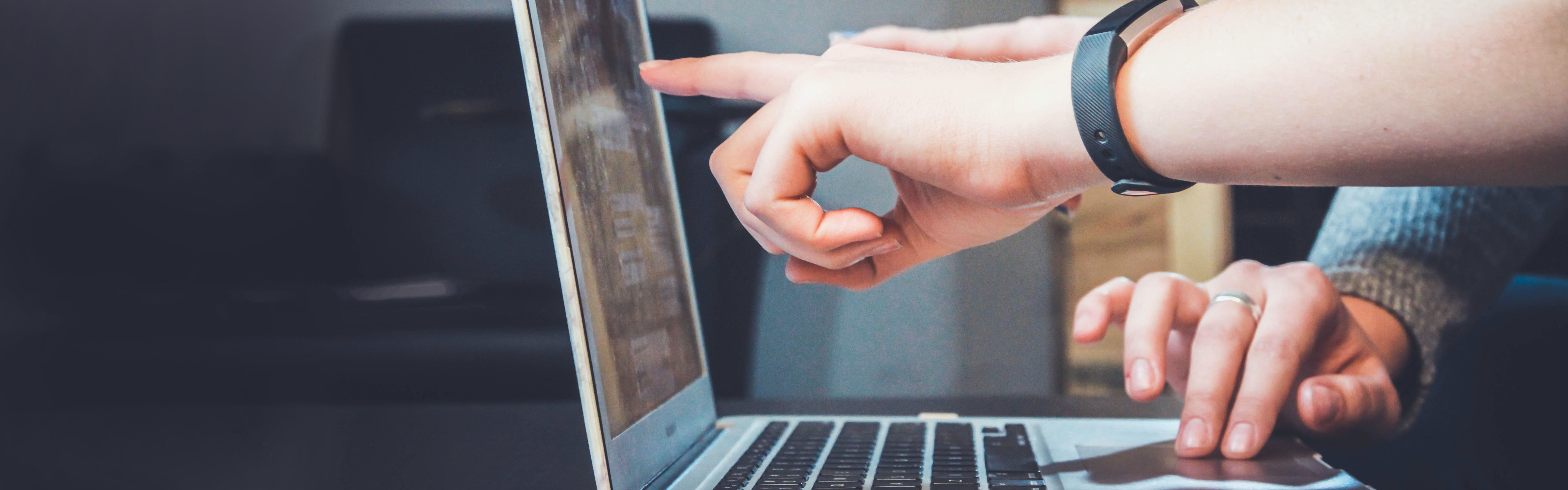 Stock photograph of persons hand pointing at a laptop screen, another hand rests on the keyboard