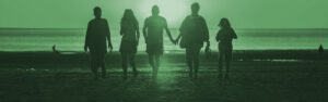 tinted green photograph of 5 silhouetted family members walking into the sun on a beach