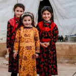 Stock photograph of 3 young Syrian children standing in a camp