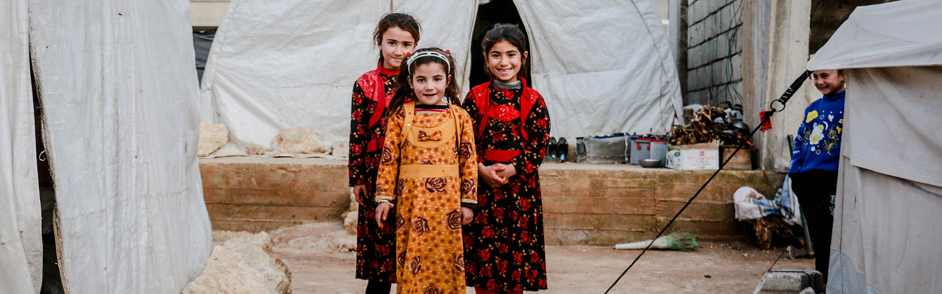 Stock photograph of 3 young Syrian children standing in a camp