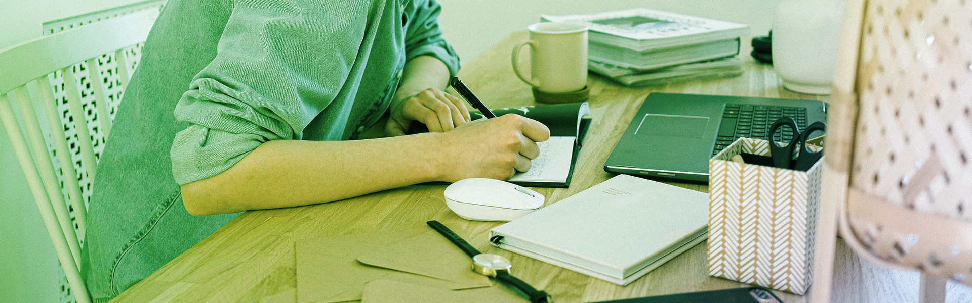 Stock photograph of a woman writing notes on a desk at a computer