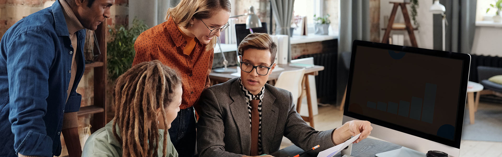 A Group of People Discussing Beside a Desktop with Graph on Screen