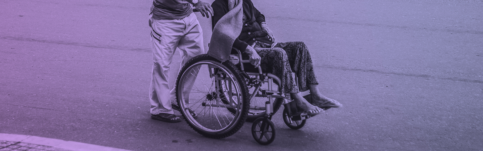 Cropped Stock photograph of a man pushing a person in a wheelchair on a tarmac road