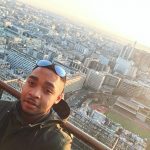 Photograph of Tyrone looking at the camera with a view of a city behind him